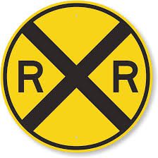 Yellow circular railroad crossing sign with a large black "X" and the letters "R" on either side, warning of railroad crossings ahead.